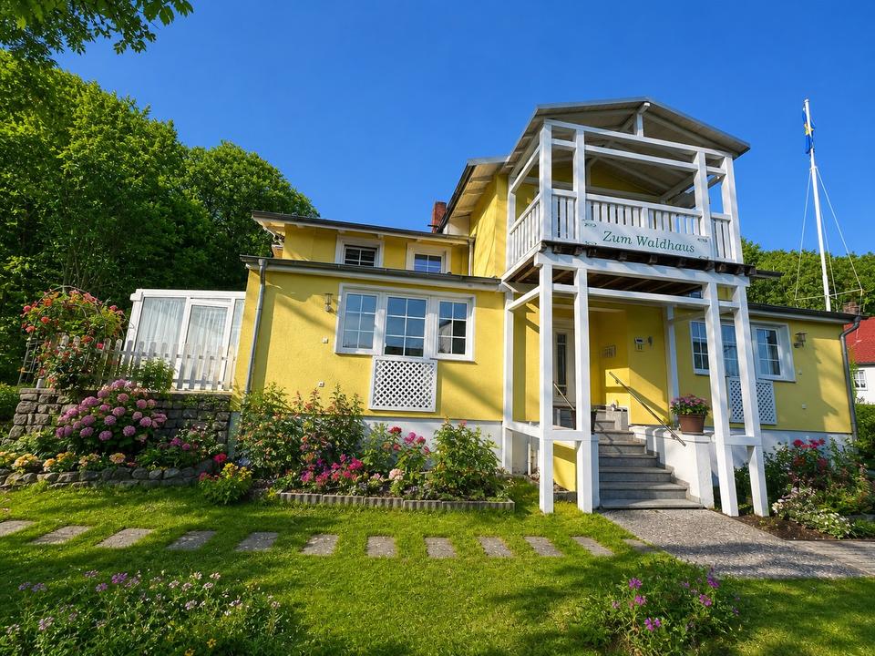 Frontansicht des Waldhauses Sellin mit weißen Balkonen, blühenden Hortensien und sonnigem Garten